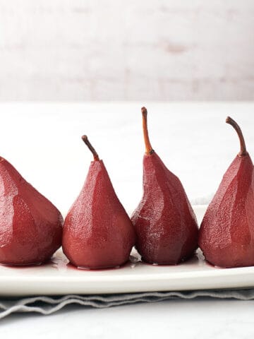 side view of 4 poached pears in red wine on white rectangular platter with grey napkin underneath