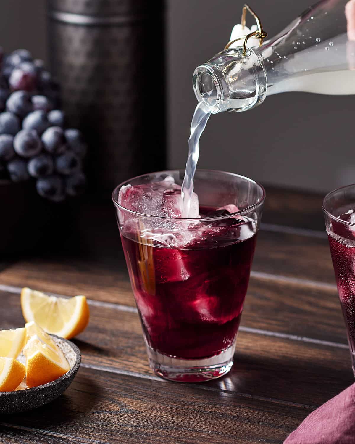 Side view of pouring lemon soda over red wine in a glass with ice to make a red wine spritzer.