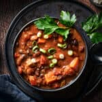 Top down shot of chili in bowl on plate on wood surface.