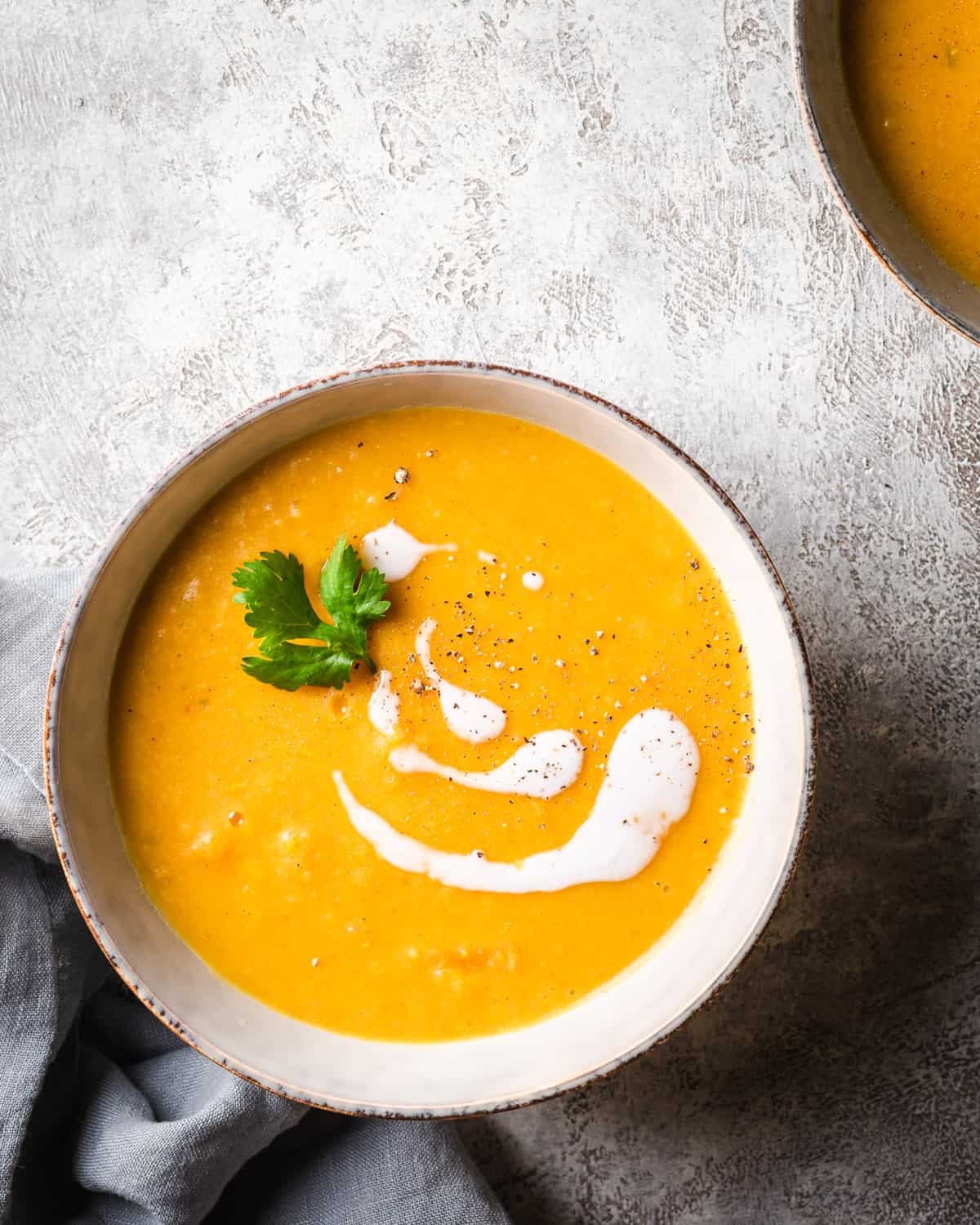 bowl of orange soup with cilantro and coconut cream and grey napkin