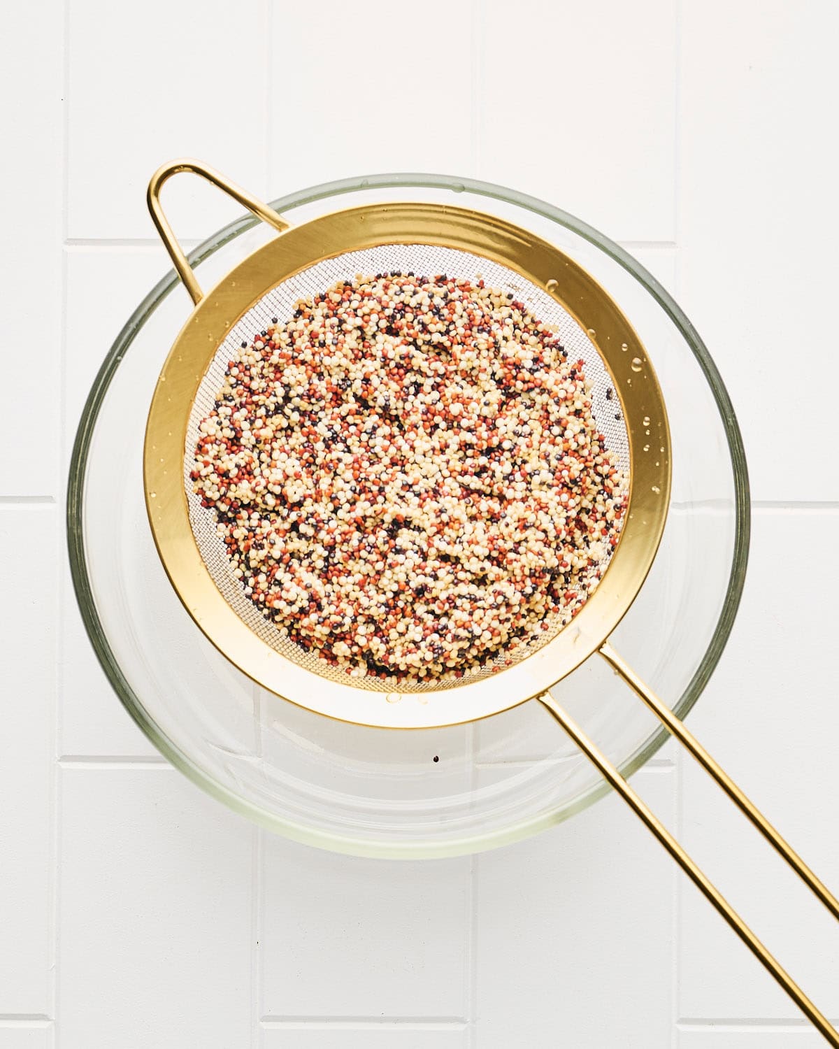 Rinsing quinoa in a sieve over a glass bowl.