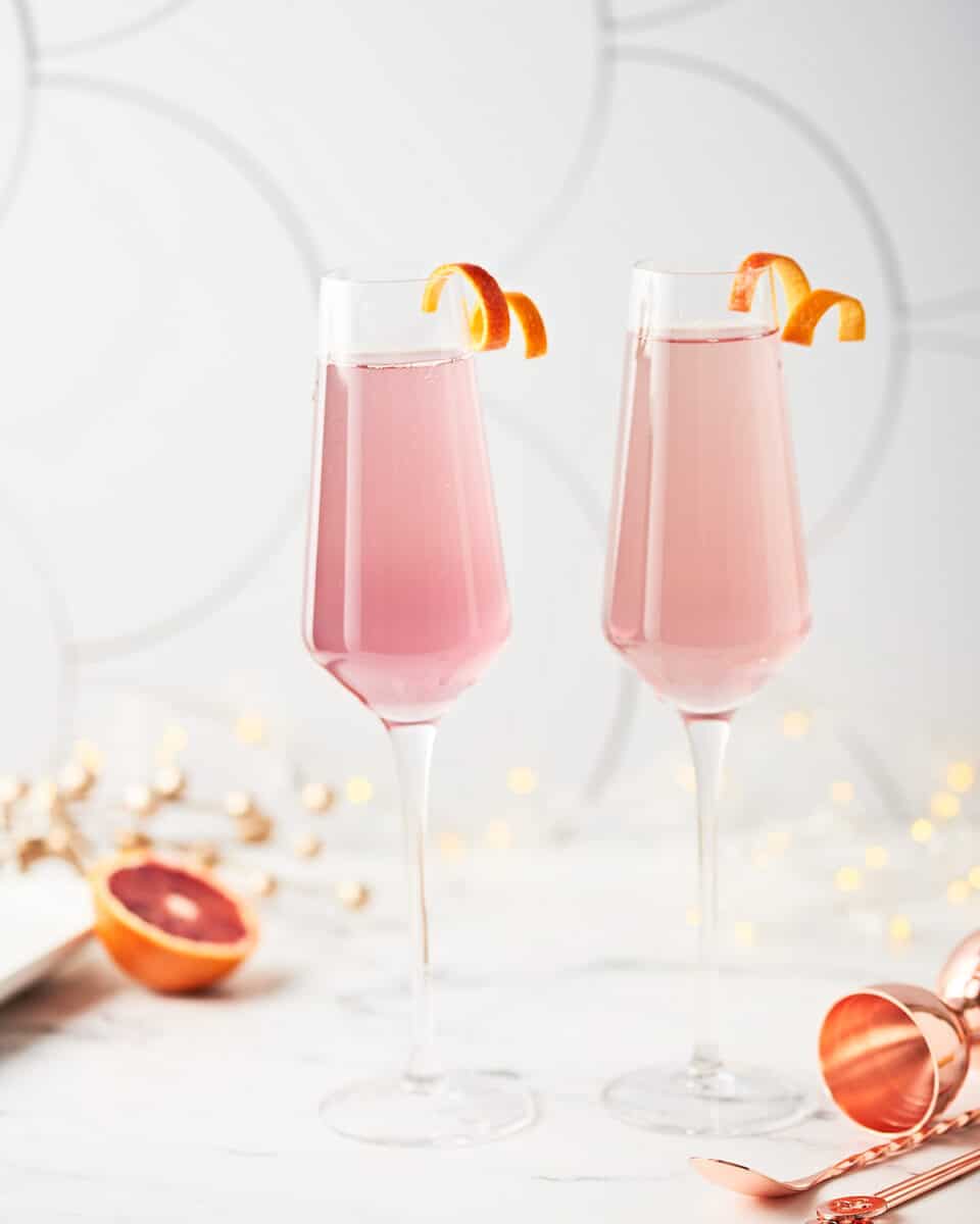 side view of 2 champagne fluites filled with blood orange French 75 with orange twists