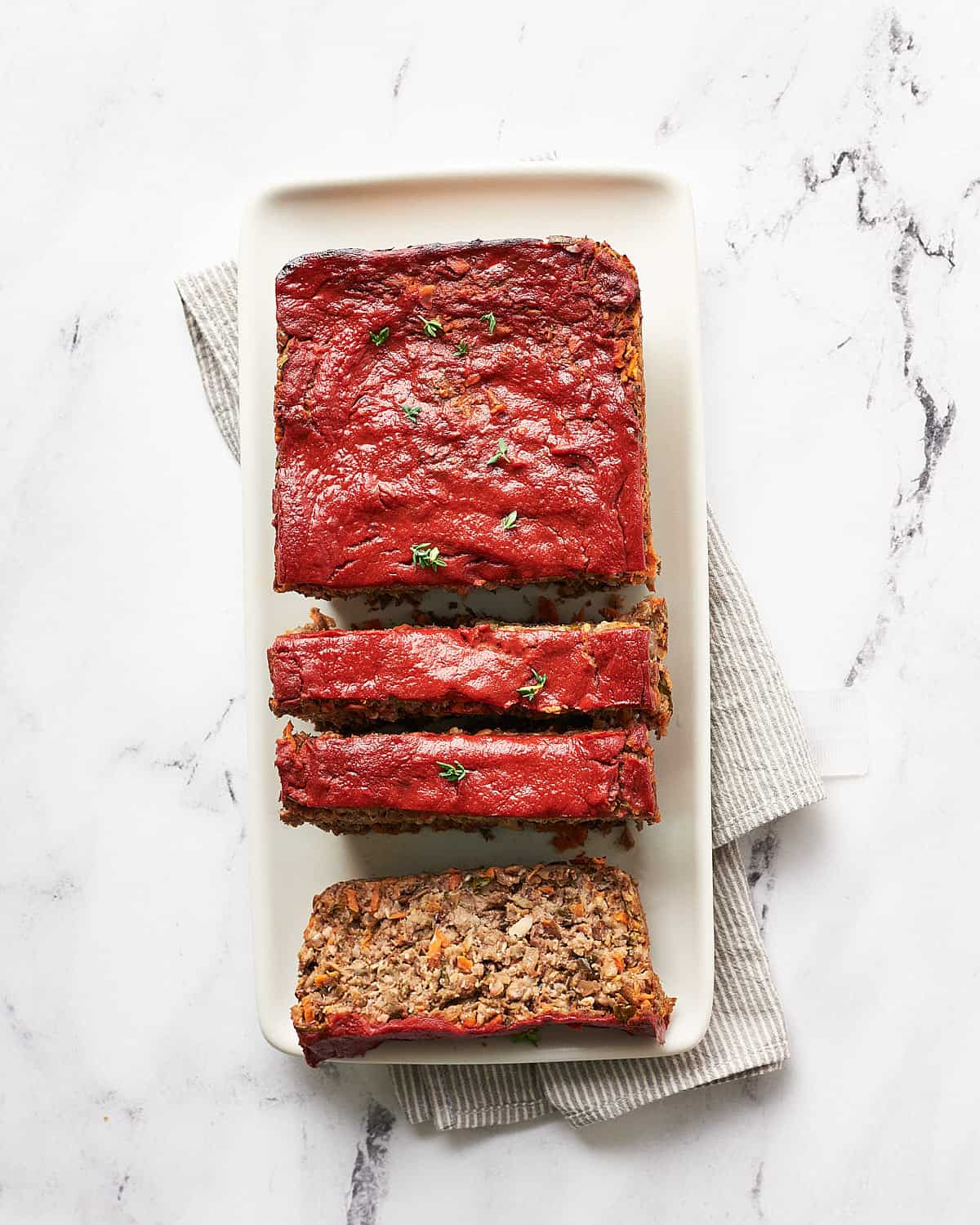 top view of sliced vegan meatloaf on a white platter on marble background