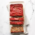 overhead view of vegan meatloaf sliced on a white platter on a marble background with grey and white striped napkin