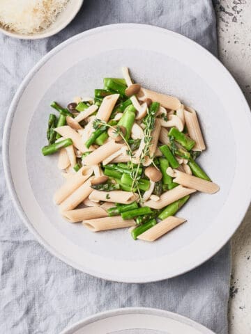 Bowl of Asparagus Mushroom Pasta on grey background with glass of wine.