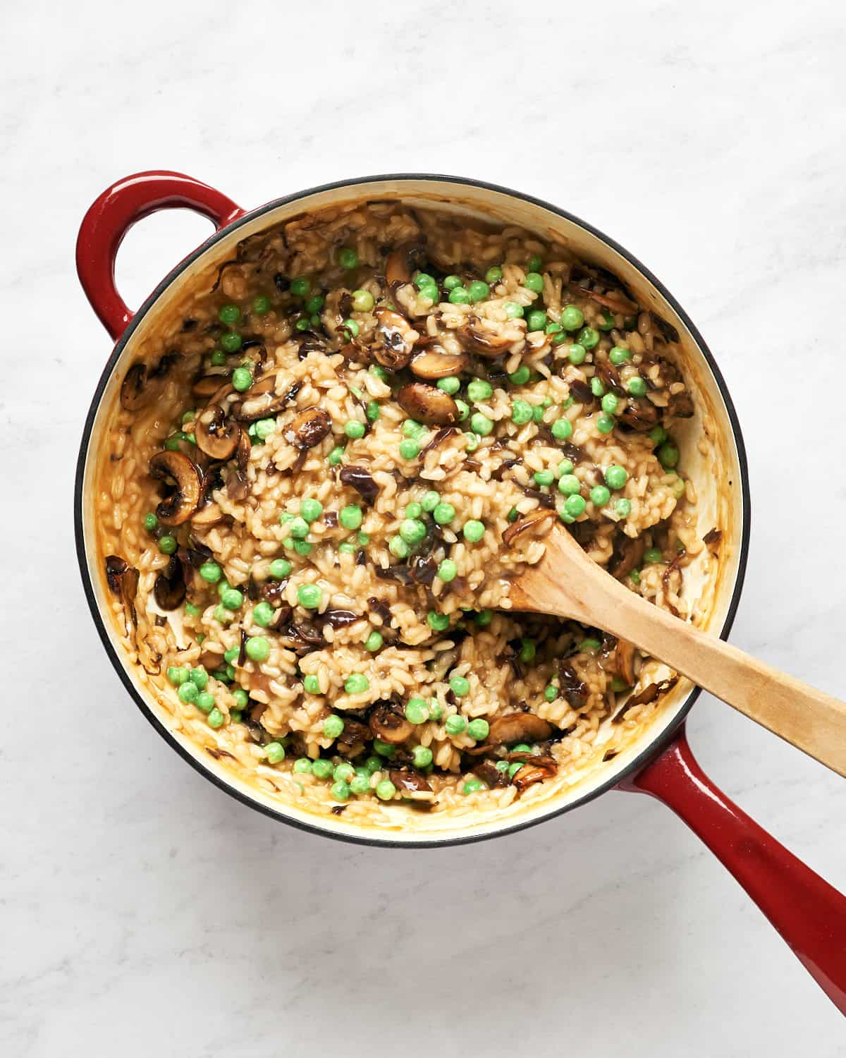 Stirring peas and mushrooms into risotto in saucepan on marble background