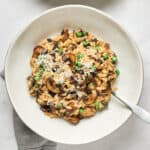 White bowl with vegan Mushroom Risotto with peas with spoon and grey napkin