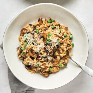 White bowl with vegan Mushroom Risotto with peas with spoon and grey napkin