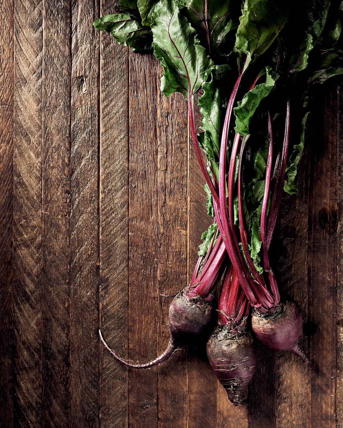 3 beets with beet greens on wooden background
