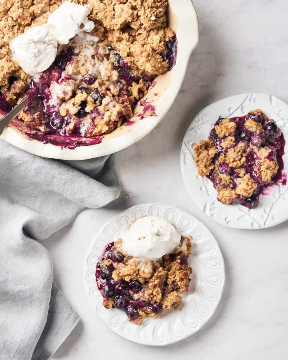 Two plates of vegan blueberry cobbler with dairy free ice cream and pie dish