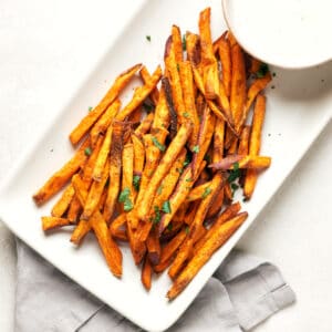 White tray with fresh baked healthy sweet potato fries on white platter with vegan ranch dip