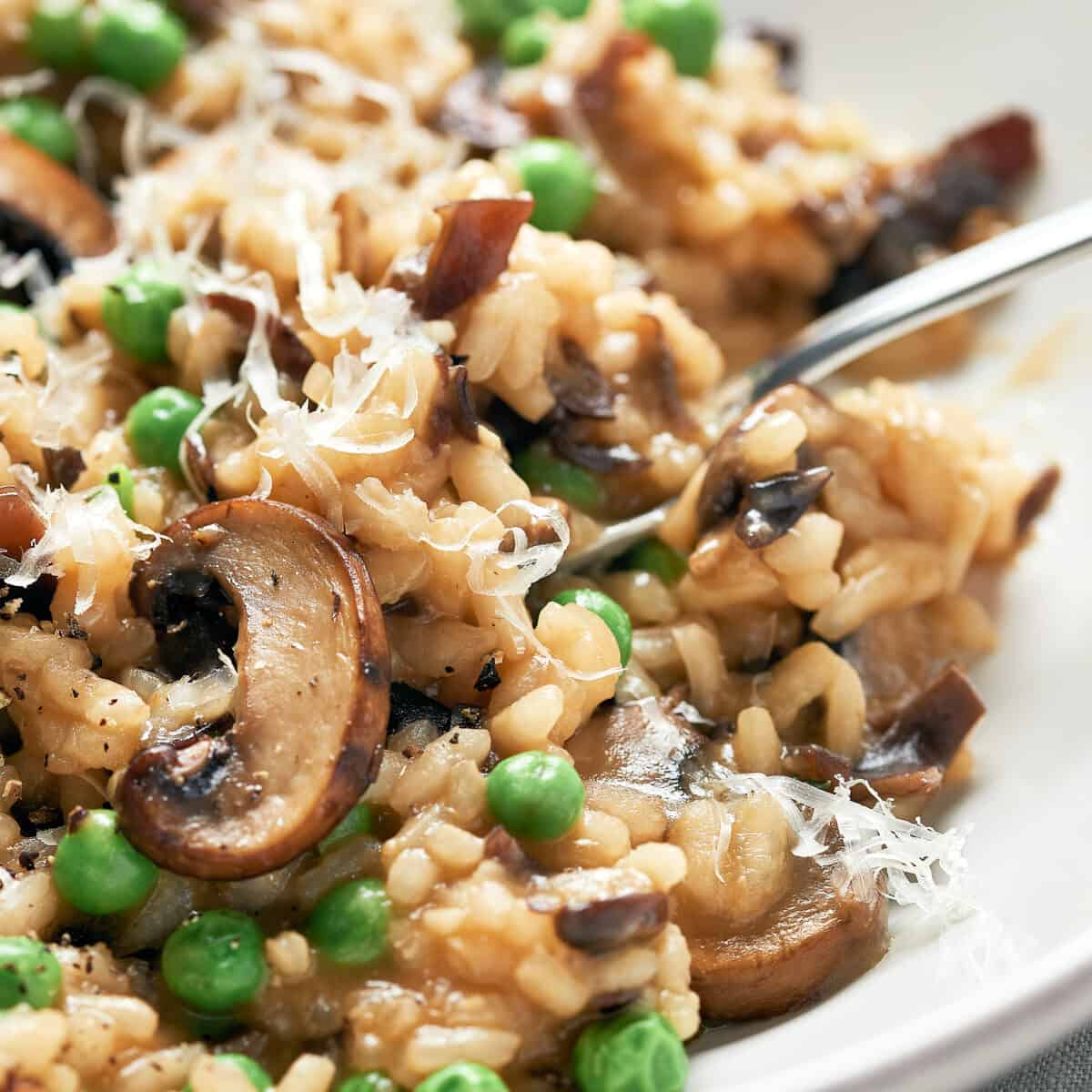 closeup of creamy vegan mushroom risotto with peas with fork on white plate
