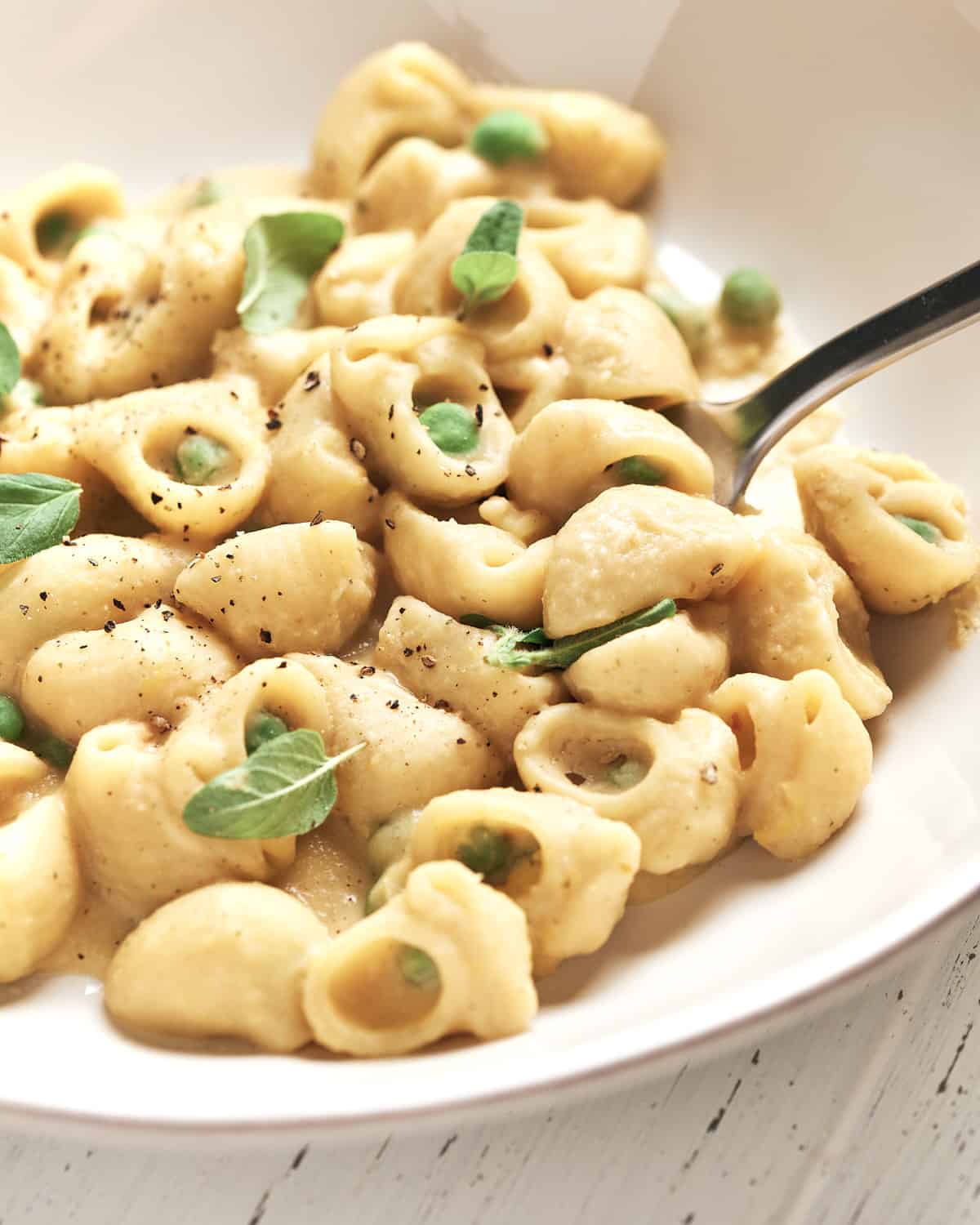 close view of creamy vegan pasta with peas on white plate with fork