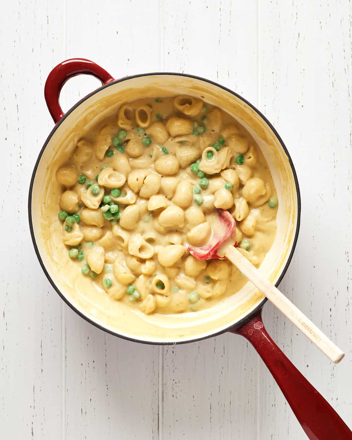 Saucepan with pasta, bean sauce, peas with spatula on white wood background.