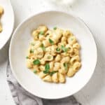 Pasta with peas in white bowl on white wood background.