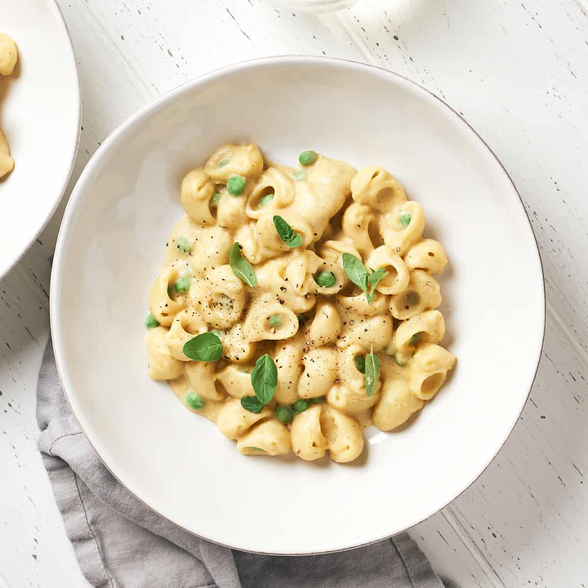 Pasta with peas in white bowl on white wood background.