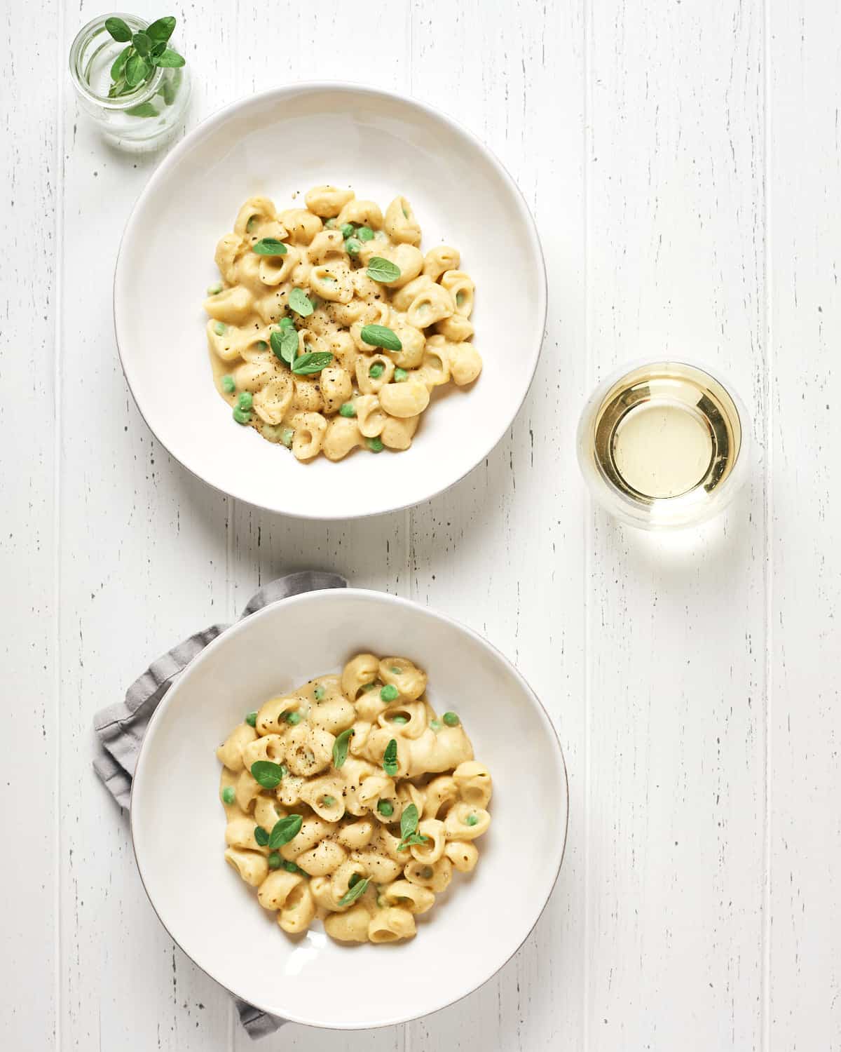 pasta with peas served in bowls with glass of white wine on white wood background
