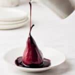 Red wine sauce poured over red wine poached pears on white plate