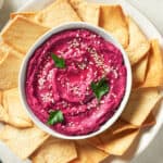 white bowl with roasted beet hummus with pita chips on white plate