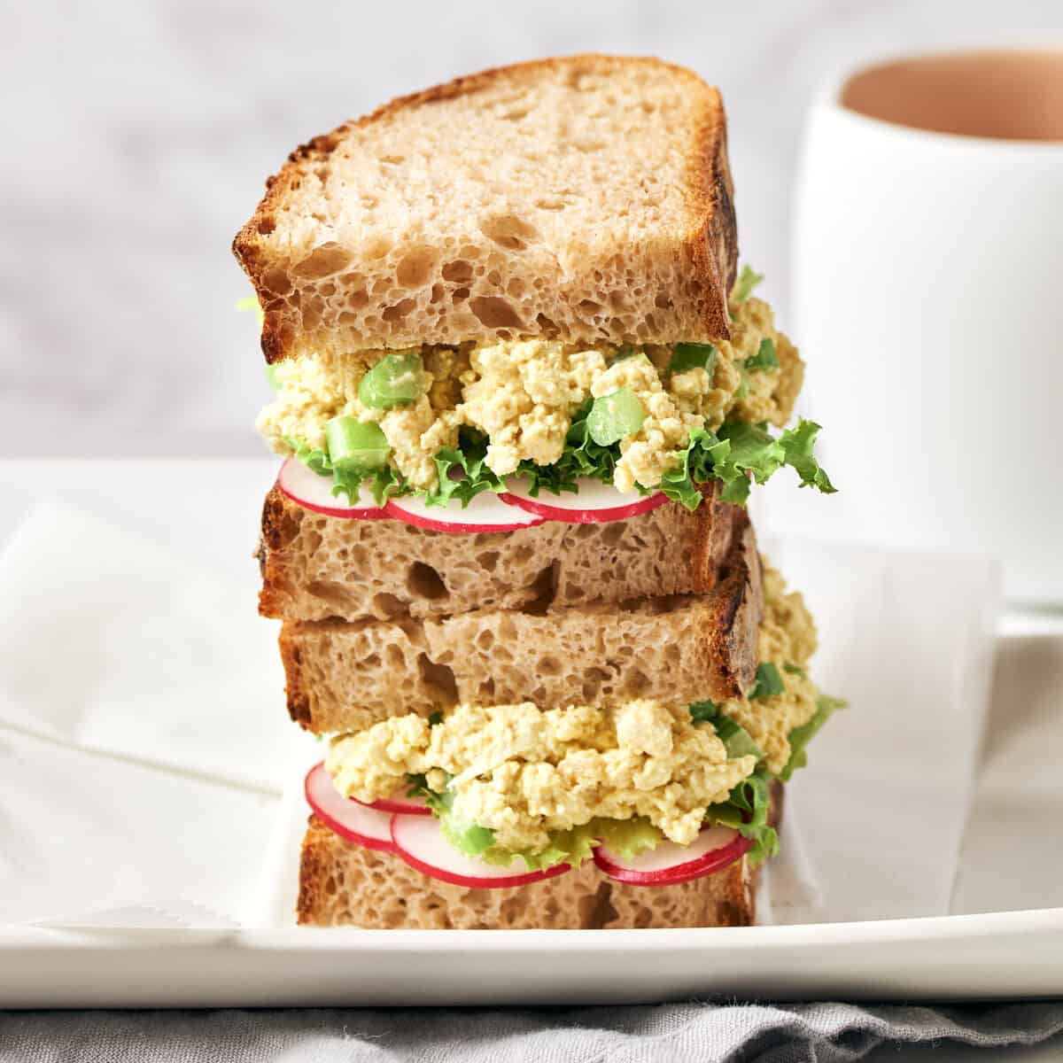 Tofu salad sandwiches on white platter with grey napkin