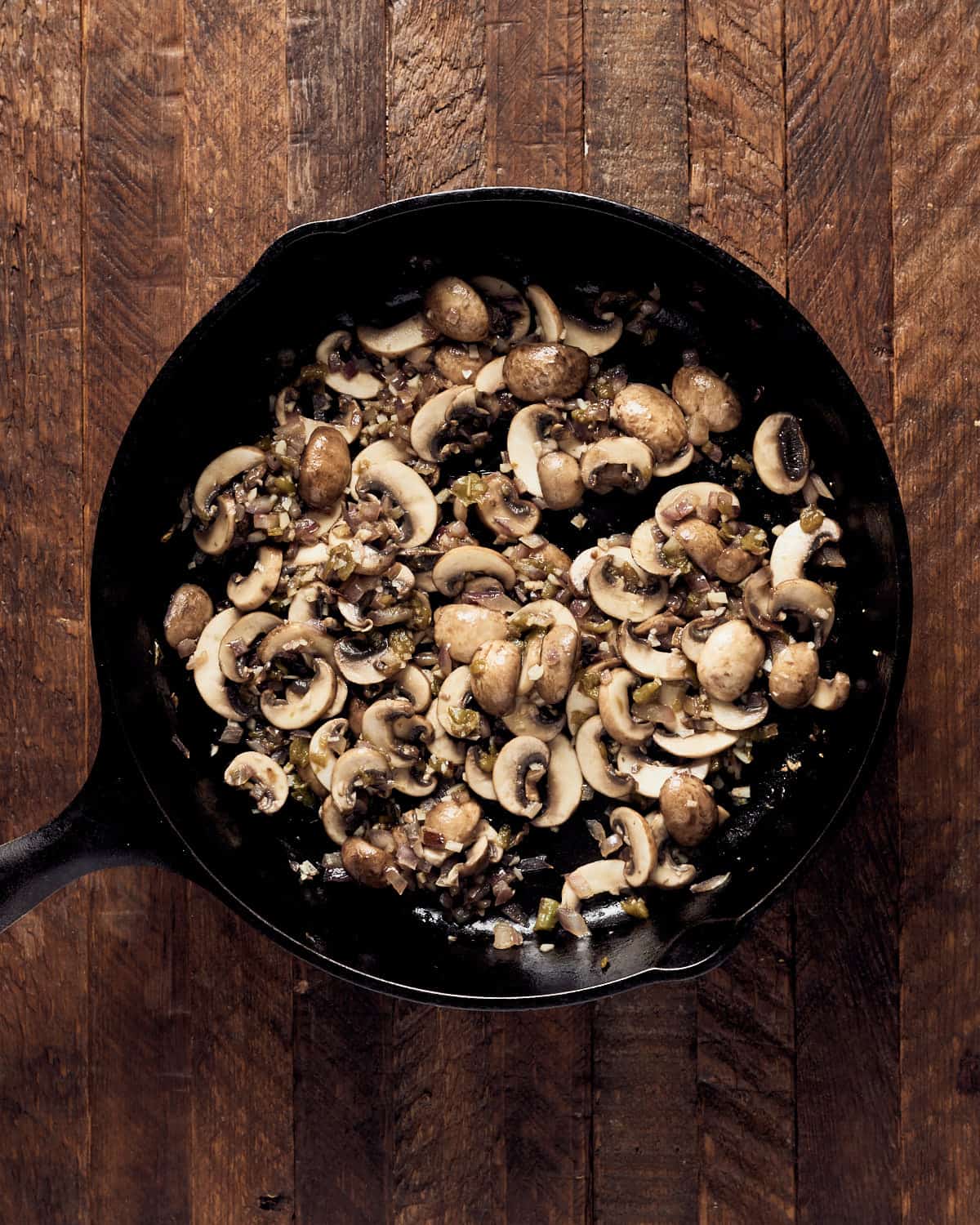 Cooking mushrooms with onions and garlic in cast iron pan on wood background
