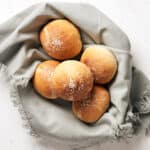Top view of five burger buns in a bowl on a grey napkin.