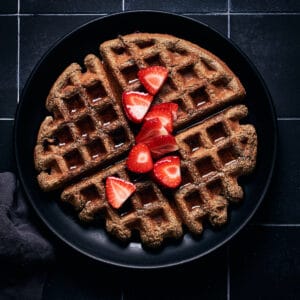 Overhead view of plate of waffles with strawberries and maple syrup on top.