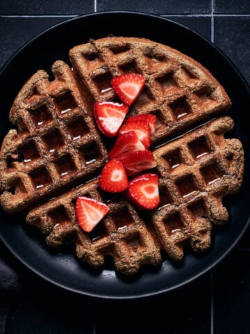 Overhead view of plate of waffles with strawberries and maple syrup on top.