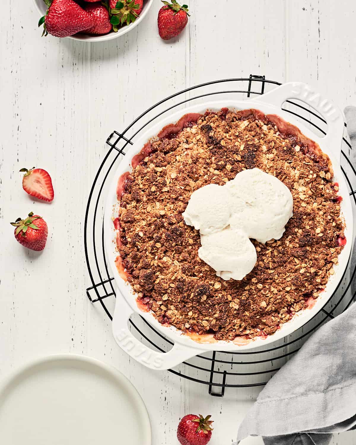 Top view of vegan strawberry Rhubarb Crisp on white wooden background.