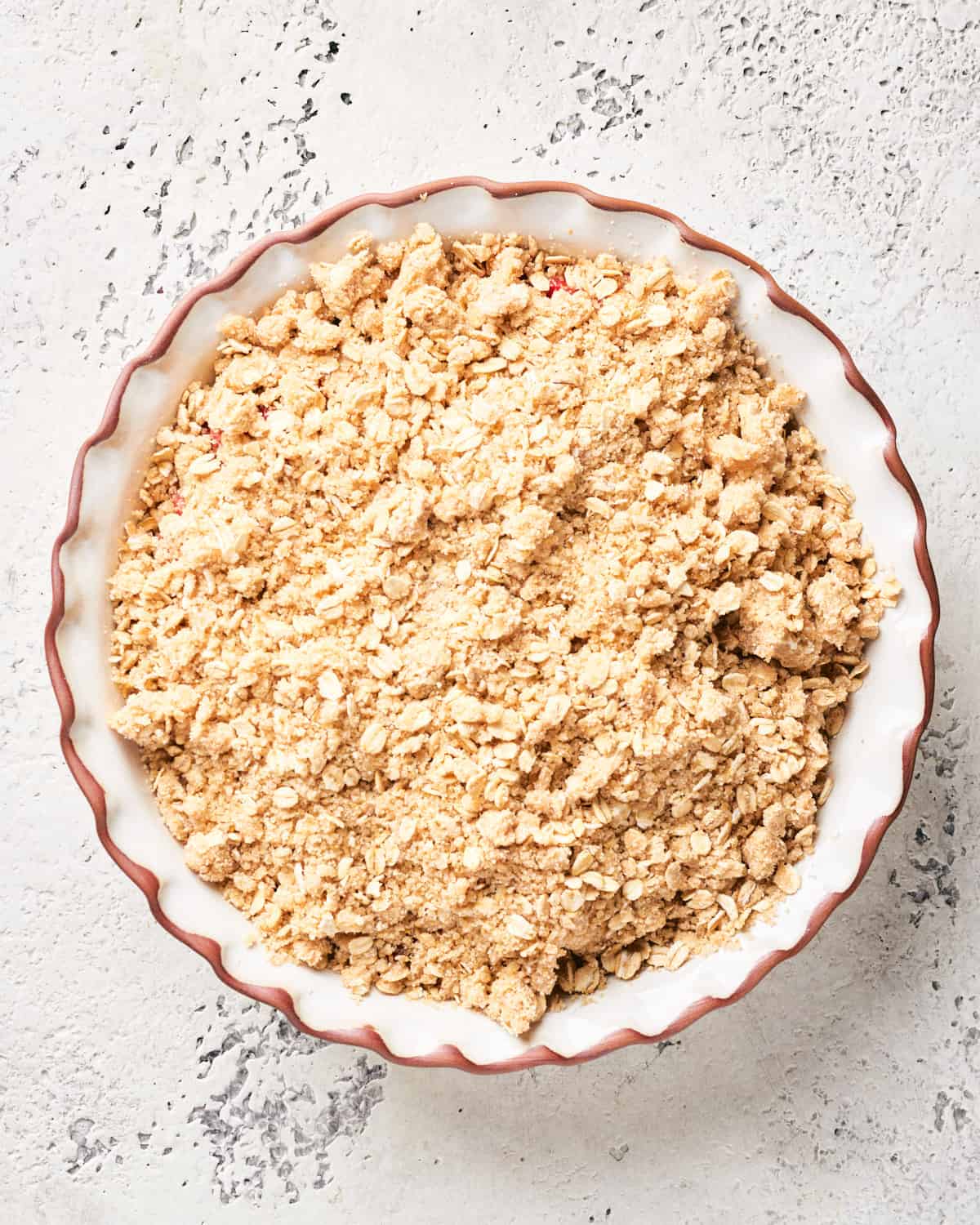 Crisp topping placed on fruit filling in white pie plate.