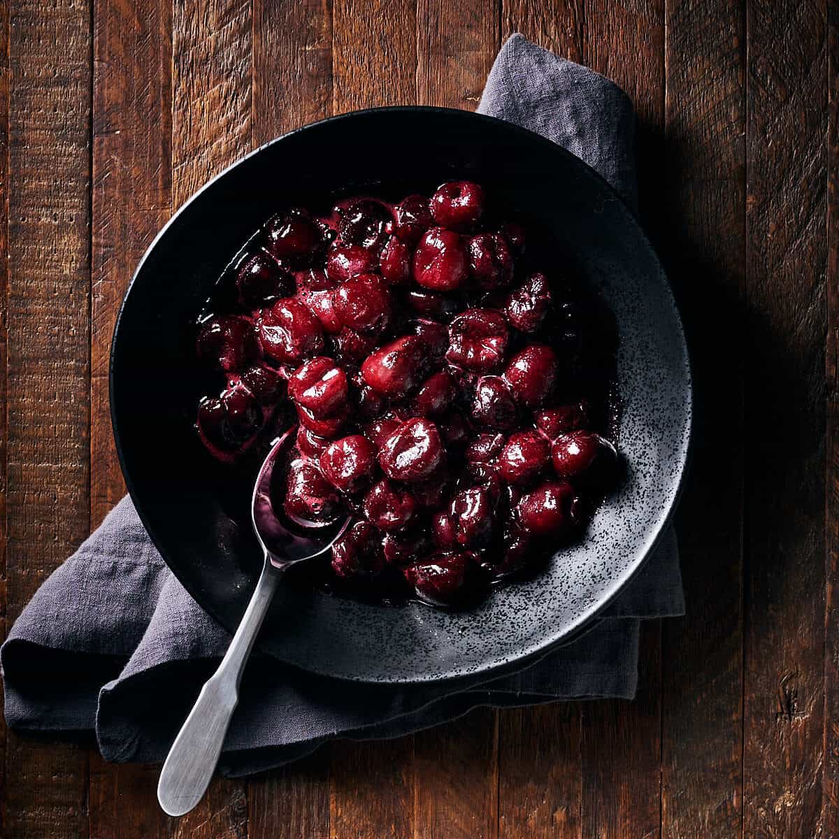 Overhead view of cherry compote in black bowlon wood background.