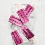 Overhead view of cherry coconut popsicles on top of ice cubes on white tray.