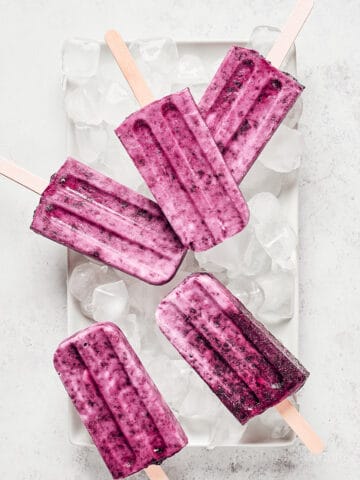 Overhead view of cherry coconut popsicles on top of ice cubes on white tray.