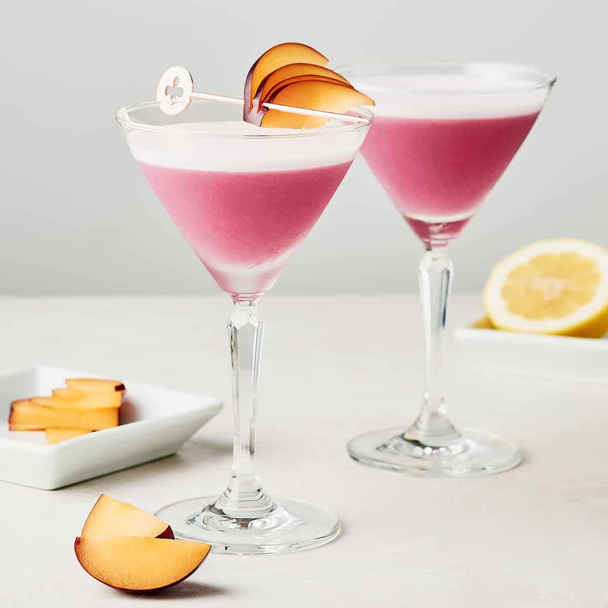 Side view of two glasses of plum ginger gin sour on grey surface.