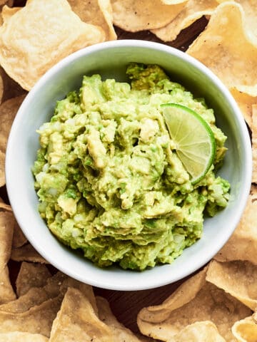 Top down view of 4 ingredient guacamole in white bowl with tortilla chips.