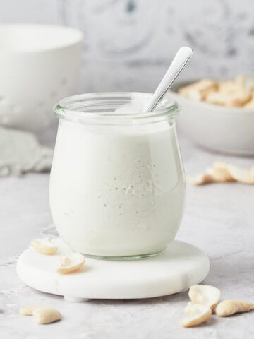Side view of cashew cream in glass jar with spoon.