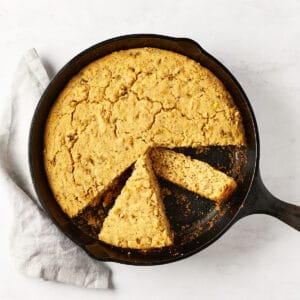 Overhead view of vegan southwest skillet cornbread in cast iron skillet on marble surface with grey napkin.