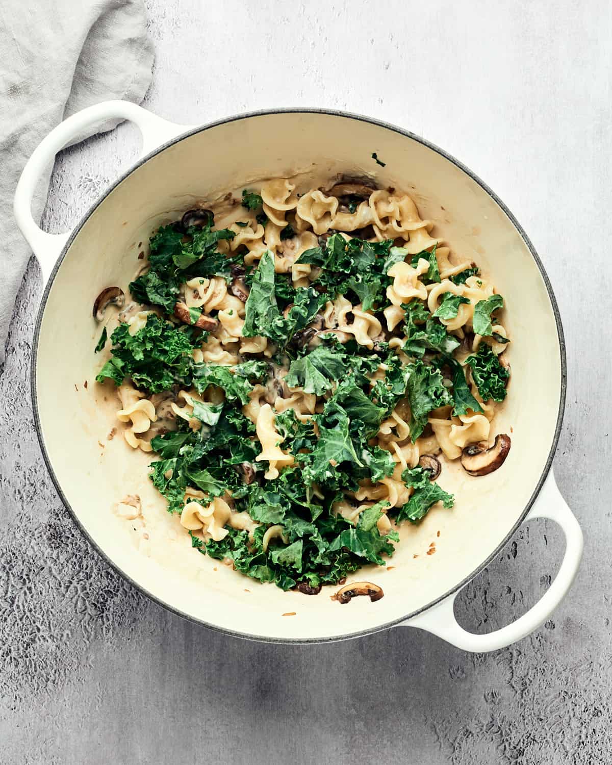 op view of kale, mushrooms, and pasta in saucepan.