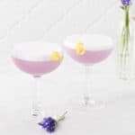 Side view of two lavender elderflower gin sour cocktails on marble surface.