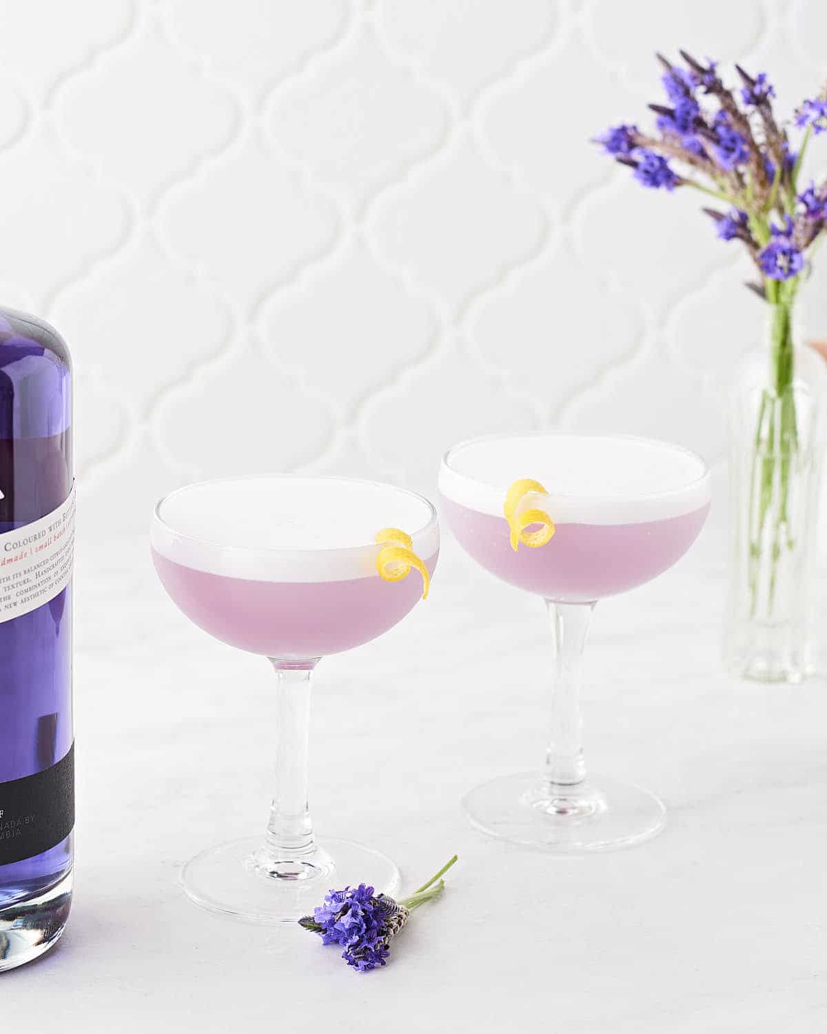 Side view of two lavender elderflower gin sour cocktails on marble surface.