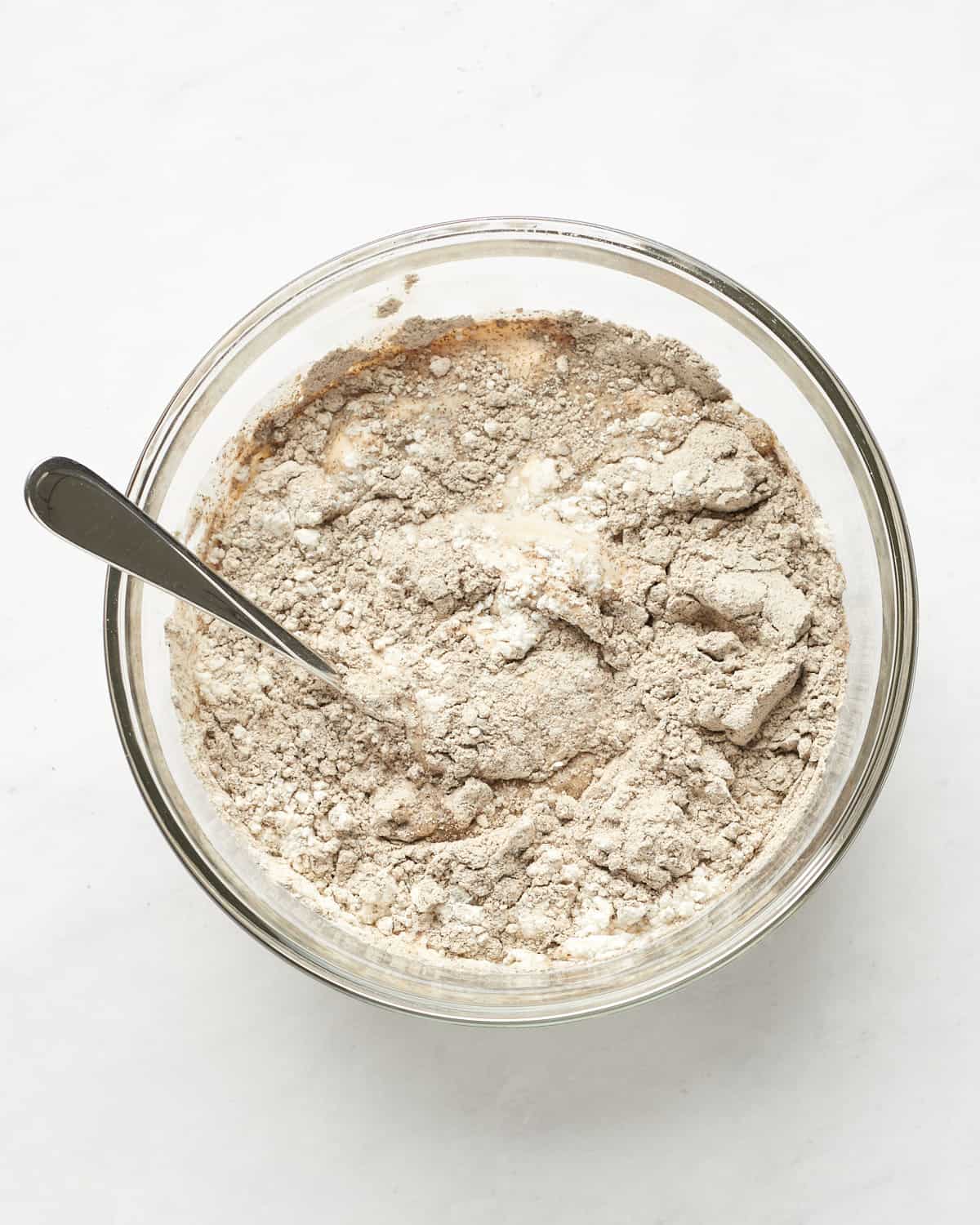 Top view of mixture of soy milk, sourdough discard, and flour in a pint glass jar with spoon on marble background.