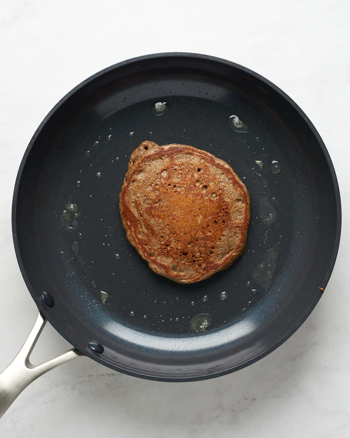 Top view of pancake on a non-stick skillet with melted vegan butter.