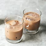 Side view of two glasses of iced vegan Irish cream on a grey textured background.