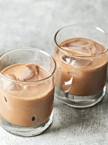 Side view of two glasses of iced vegan Irish cream on a grey textured background.