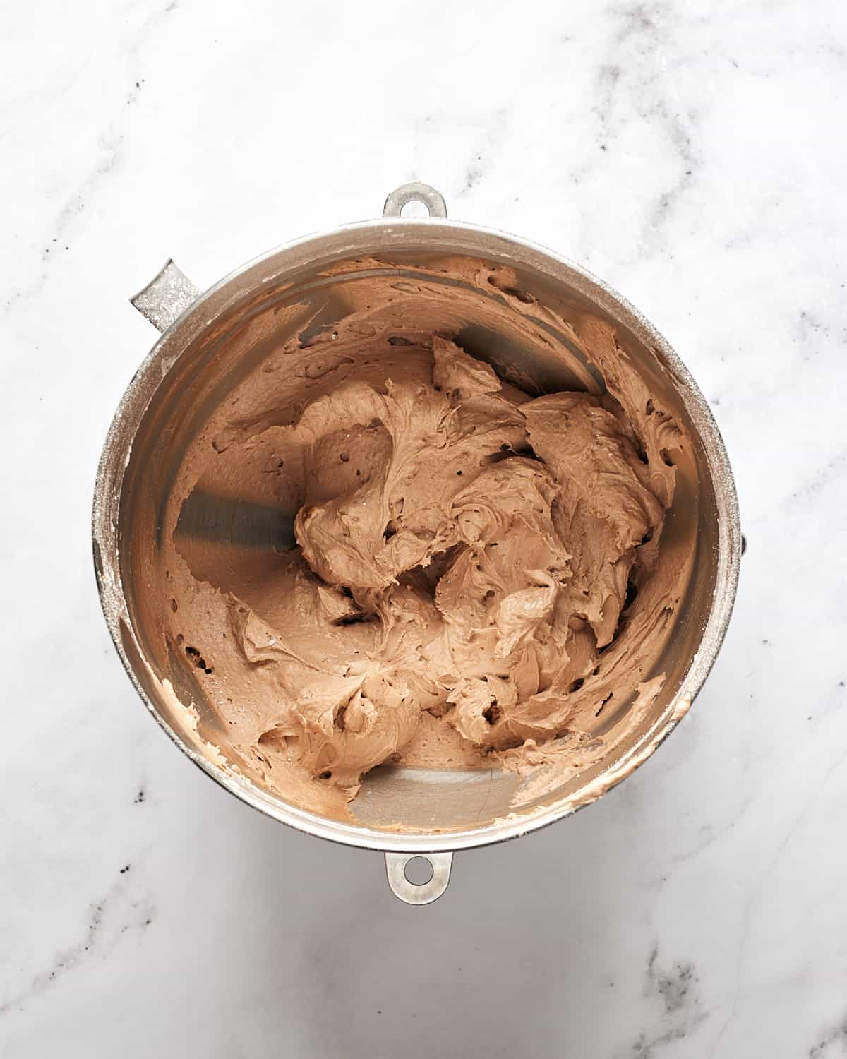 Overhead view of vegan chocoalte Irish Cream frosting in stainless steel mixing bowl on marble surface.