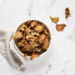 Top view of vegan cheesy kale chips with nutritional yeast in a bowl on a marble surface.