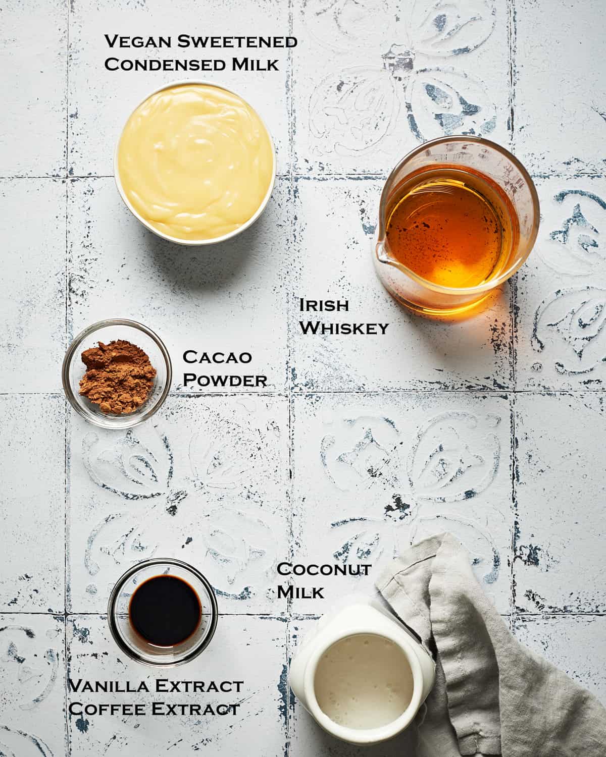 Overhead view of vegan irish cream ingredients on tile surpace with grey napkin.