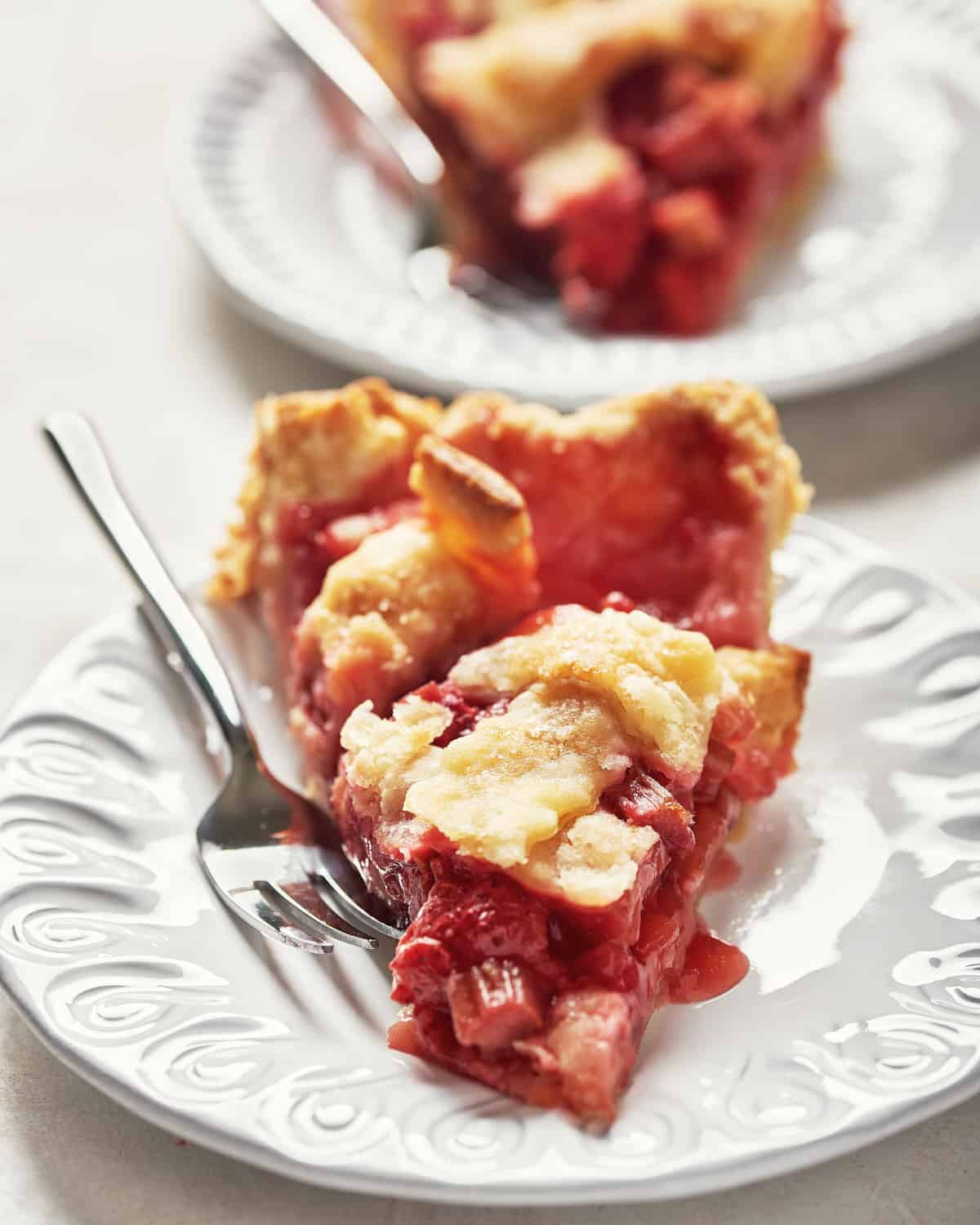 Straight on view of a slice of vegan strawberry rhubarb pie on a white plate with fork close up.