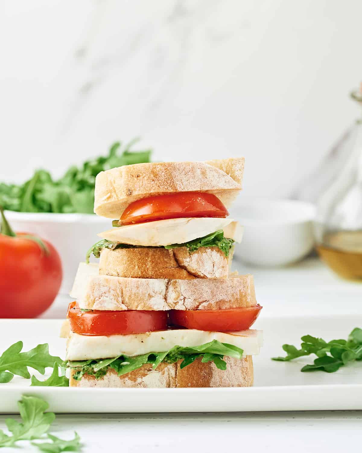 Side view of stacked Vegan Caprese Sandwich on a white plate.