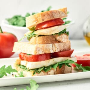 Side view of stacked Vegan Caprese Sandwich with sliced tomatoes, arugula, vegan pesto, and vegan mozzarella.